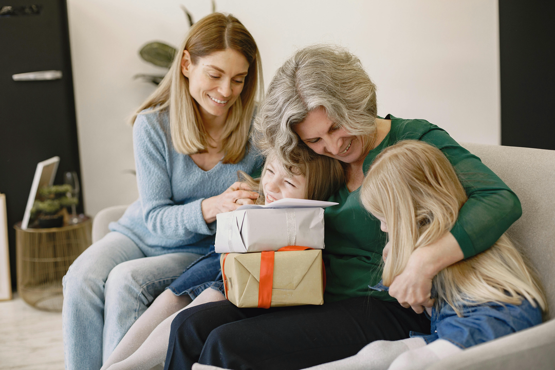 A heartwarming scene of a multi-generational family sharing a moment of connection on a sofa, featuring a grandmother in a green top warmly embracing her two young granddaughters