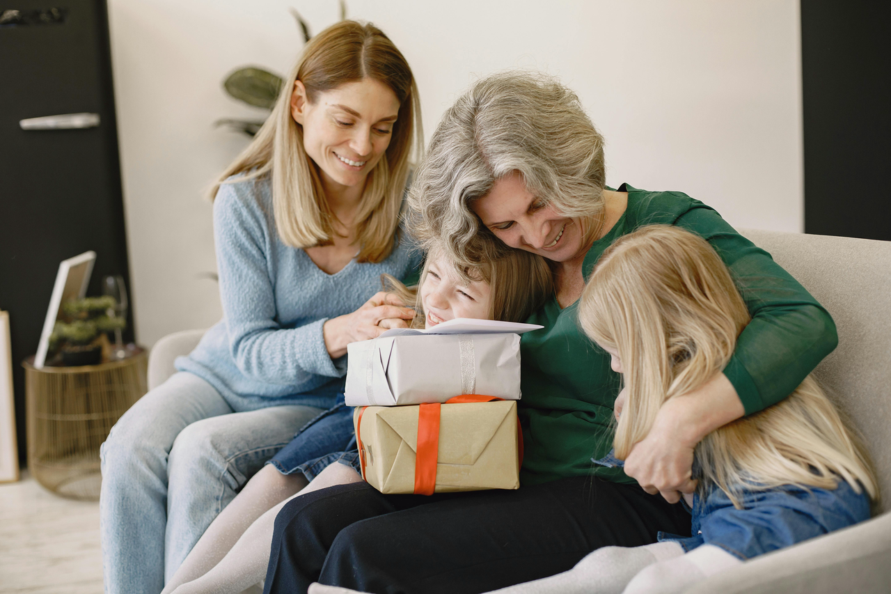 A heartwarming scene of a multi-generational family sharing a moment of connection on a sofa, featuring a grandmother in a green top warmly embracing her two young granddaughters