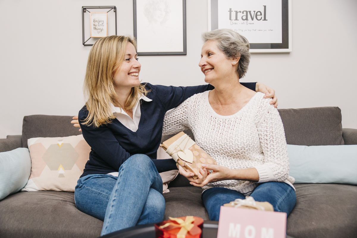 A daughter presenting a heartfelt mother necklace to her mom in a cozy living room.